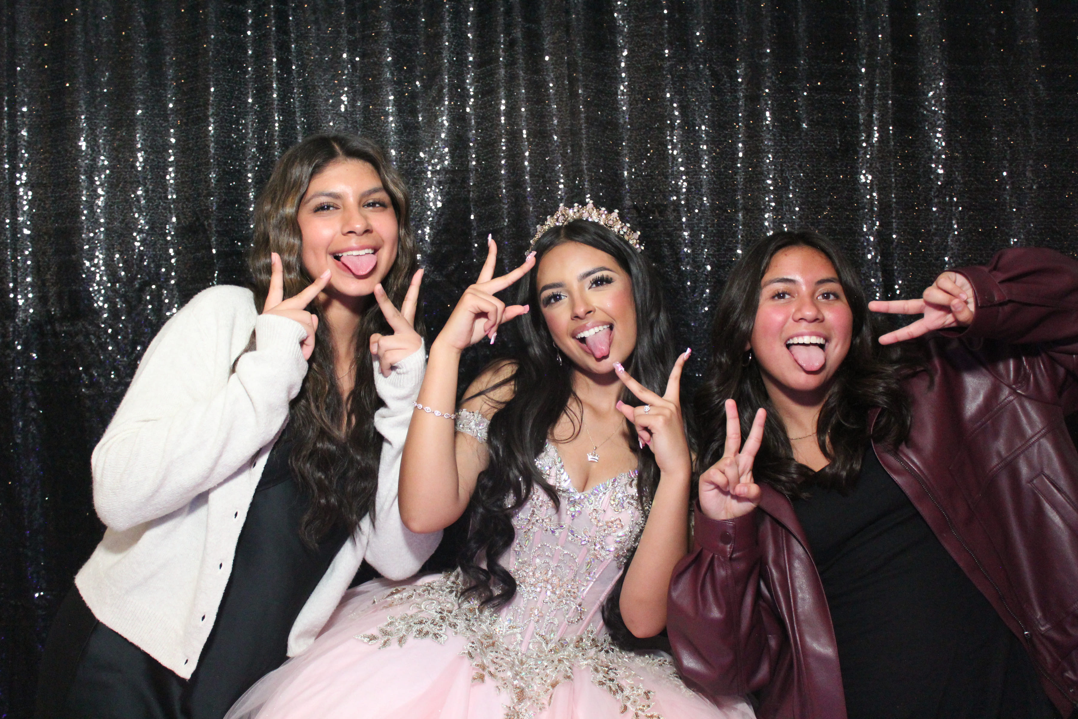 Quinceañera with friends making peace signs on sequin backdrop