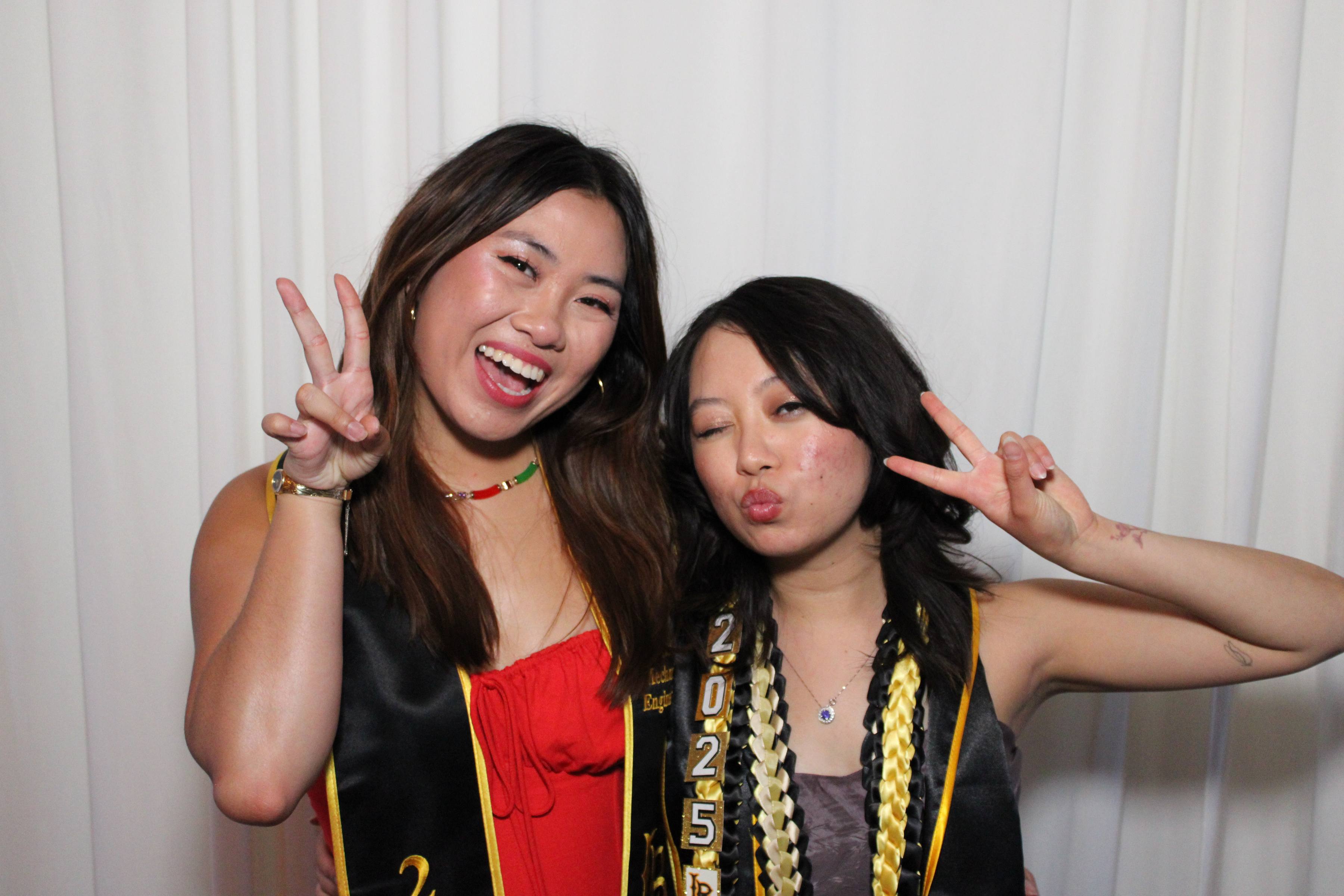 Two graduates with Class of 2025 sashes throwing peace signs